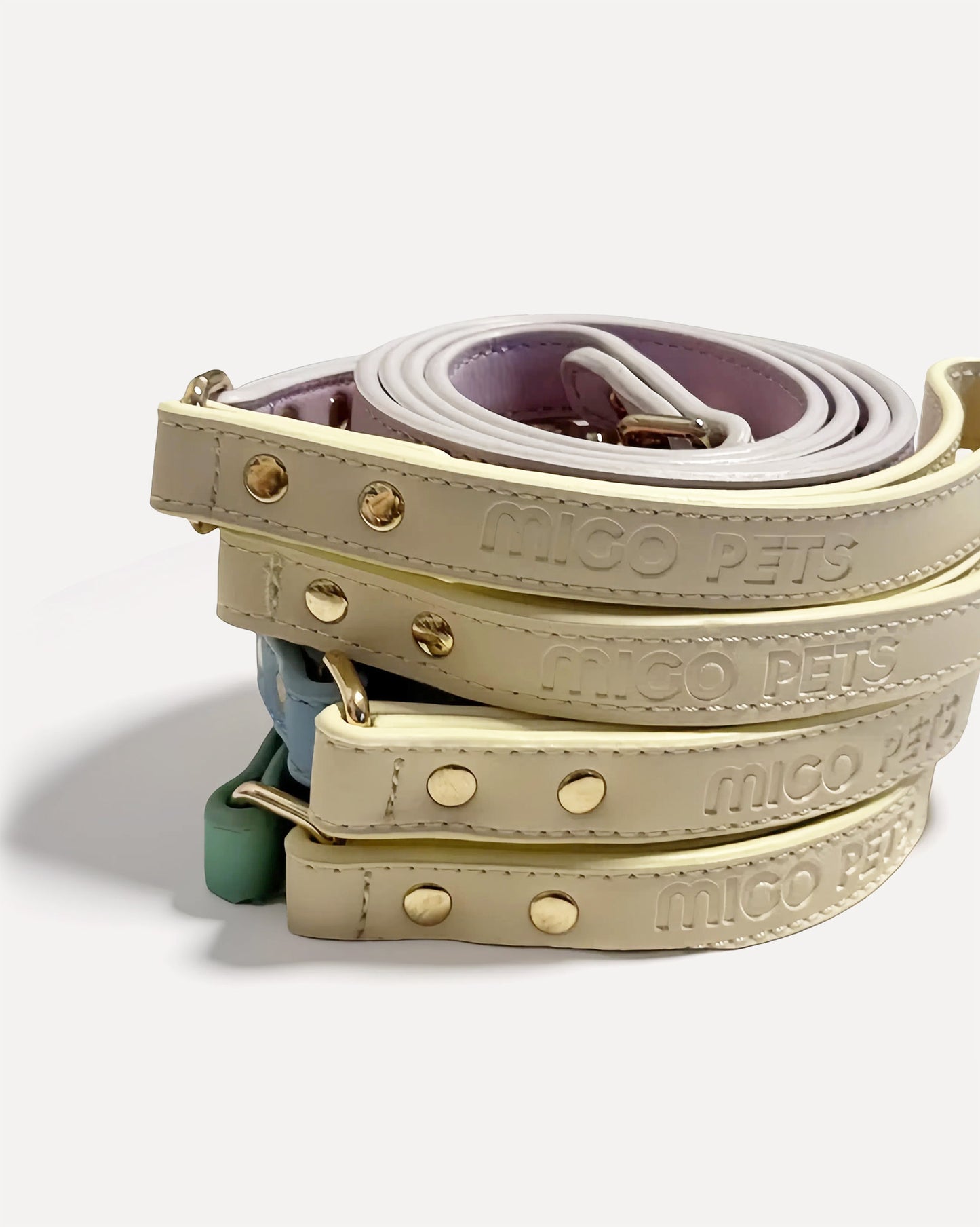 Stacked eco-friendly two-tone leather dog leashes in cream color with 'MIGO PETS' embossed branding and gold hardware.