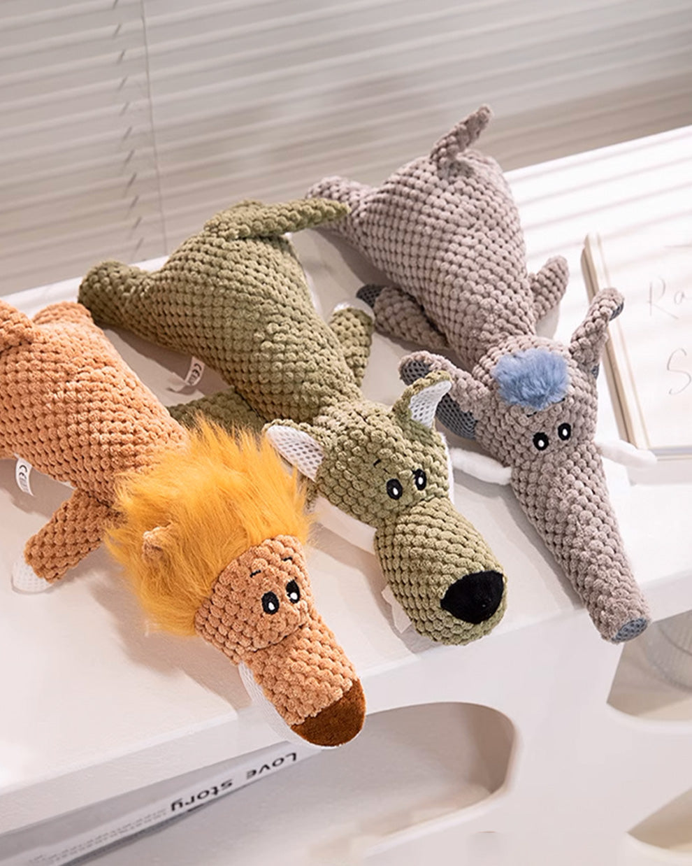 Side view of three squeaky toys, including a lion, wolf, and elephant.